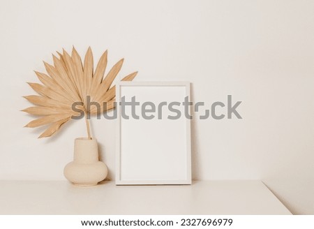 Aesthetic photo frame mockup with vase and palm leaf on wooden white table. Picture frame template with copy space for poster and design, stylish home interior decoration, scandinavian style