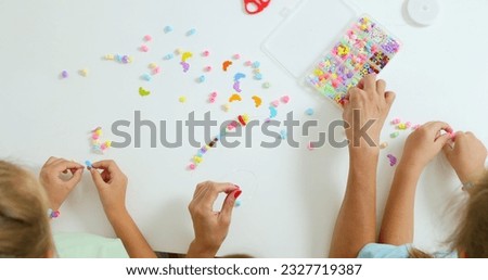Happy mother with her daughters making beaded jewelry at home Royalty-Free Stock Photo #2327719387
