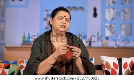 An aged Hindu woman chanting hymns Mantras - religious faith concept. An Indian lady wearing a shawl stole counting wooden beads while doing her daily prayers at home - spirituality Royalty-Free Stock Photo #2327730623