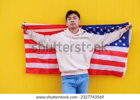 Vibrant photo of a Chinese man proudly posing with a US flag, set against a yellow wall, creating a striking and colorful composition