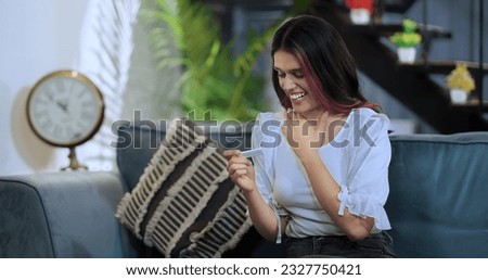 Beautiful Indian woman sittiing on sofa holding pregnancy test stick look surprise enjoy positive result feel excited for motherhood. Happy overjoyed female expecting baby after ivf treatment at home Royalty-Free Stock Photo #2327750421