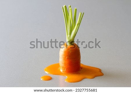 Fresh carrot with green stem melting in puddle of carrot juice, creative vegetable concept Royalty-Free Stock Photo #2327755681
