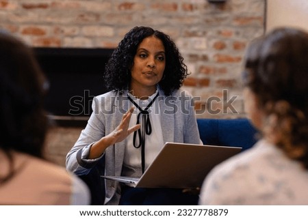 Diverse female colleagues in discussion using laptop in casual office meeting. Casual office, teamwork, business, lifestyle, communication and work, unaltered.