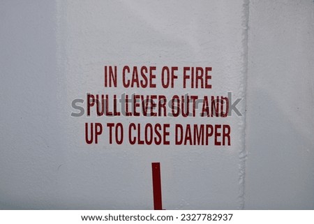 A sign on the wall that says "In case of fire pull lever out and up to close damper".