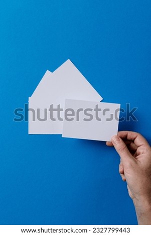 Vertical image of hand of caucasian woman with business card with copy space on blue background. Business, business card, stationery and writing space concept.