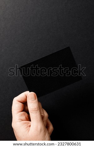 Vertical image of hand of caucasian woman with business card with copy space on black background. Business, business card, stationery and writing space concept.