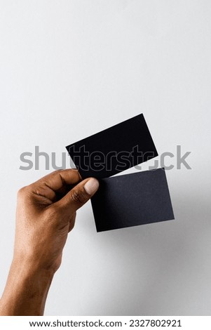 Vertical image of hand of biracial man with black business cards with copy space on white background. Business, business card, stationery and writing space concept.
