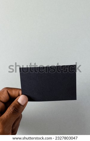 Vertical image of hand of biracial man with black business card with copy space on white background. Business, business card, stationery and writing space concept.