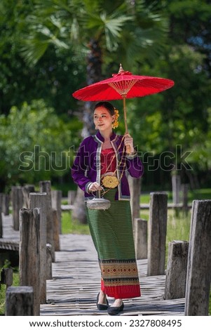 Beautiful pretty young Asian woman wearing a millionaire traditional Thai dress Lanna style standing with an antique silver bag and umbrella in a green natural park. Portrait the old fashion costume. Royalty-Free Stock Photo #2327808495
