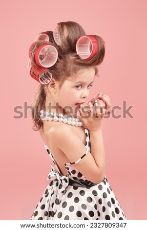 Sweets for children. Little fashionista girl dresses up for a party and eats a pink donut. Pink studio background. Kid's fashion. Pin-up style.