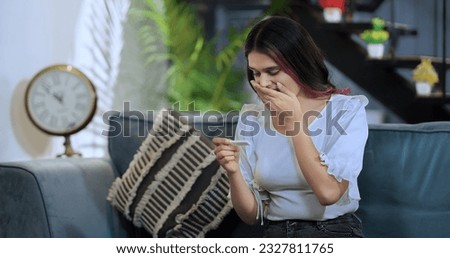 Beautiful Indian woman sittiing on sofa holding pregnancy test stick look surprise enjoy positive result feel excited for motherhood. Happy overjoyed female expecting baby after ivf treatment at home Royalty-Free Stock Photo #2327811765