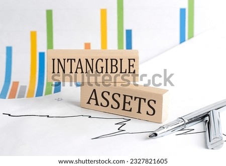 INTANGIBLE ASSETS text on wooden block on chart background, business concept Royalty-Free Stock Photo #2327821605