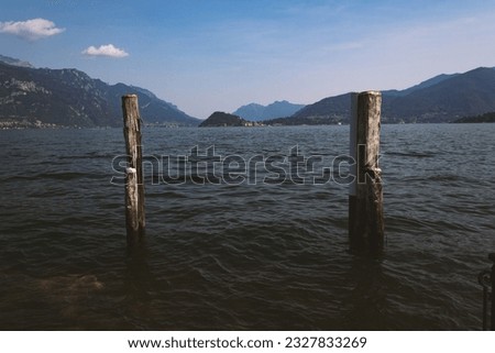 View of the town of Bellagio, the lovely and world famous village in Lake Como, Lombardy, Italy, from the town of Menaggio. Picture features wooden mooring masts, mountains, a clear summer sky.