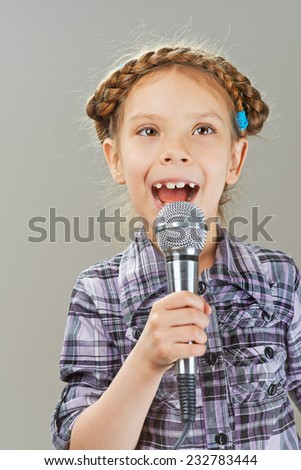 Beautiful cheerful little girl singing into microphone, isolated on gray background.