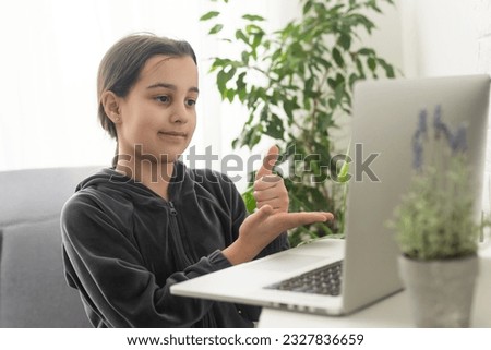 Distant education. Friendly teen girl having online lesson via laptop and showing gesturing in sign language, studying online from home