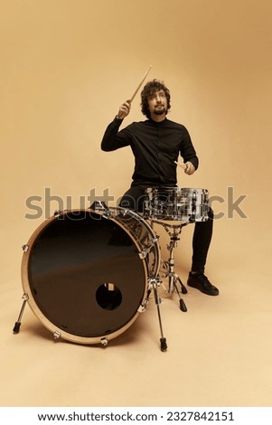 Stylish man, talented musician playing drums against light brown studio background. Lovely sounds. Concept of music, talent, hobby, entertainment, festival, performance, ad Royalty-Free Stock Photo #2327842151