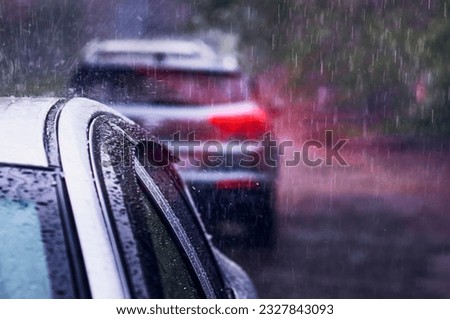 Heavy rain falls on the roof of a car during a thunderstorm. Red brake light in the dark. The concept of auto insurance and natural disasters. Driving on cloudy rainy days. Selective focus.