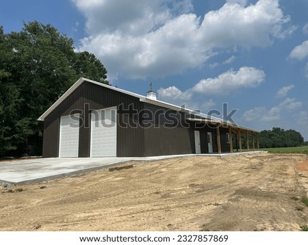 Post frame building pole barn with two roll-up doors, concrete floor, metal siding and roofing, lean-to and cupola Royalty-Free Stock Photo #2327857869
