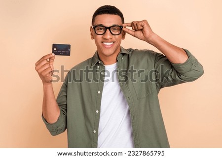 Photo of cheerful friendly handsome guy dressed khaki shirt touching eyewear hold plastic credit card isolated on pastel color background