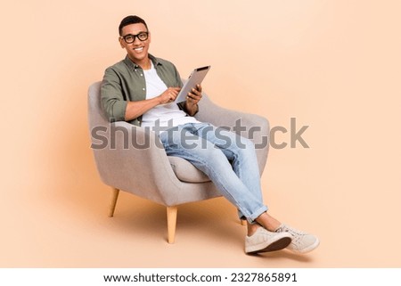 Full body portrait of cheerful young person sit comfort chair use tablet eshopping isolated on beige color background Royalty-Free Stock Photo #2327865891