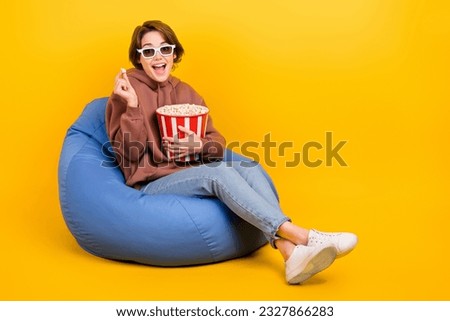 Photo of pretty positive lady sit comfort bag watch 3d glasses movie hand hold popcorn isolated on yellow color background