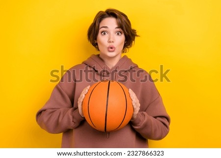 Portrait of astonished speechless girl with bob hairstyle dressed brown sportswear hold ball staring isolated on yellow color background