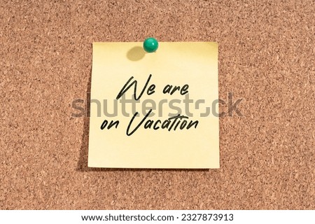 Yellow sticky note with message We are on Vacation on cork board
