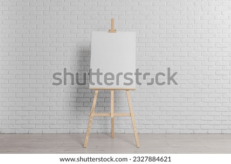 Wooden easel with blank canvas near white brick wall indoors Royalty-Free Stock Photo #2327884621