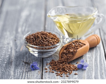Flax seeds and flax oil. Brown linen seeds, flaxseed oil and blue flax flowers on old gray wooden background. Copy space Royalty-Free Stock Photo #2327899079