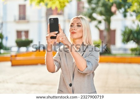 Young blonde woman making photo by the smartphone at park