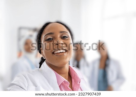 Young doctor african-american ethnicity takes a selfie, smiles with white teeth against the background of other medical colleagues. Woman hospital worker looking at camera and smiling