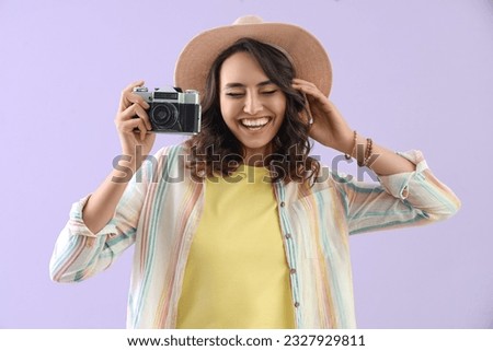 Young woman in summer hat with photo camera on lilac background