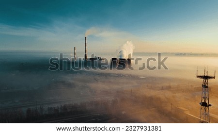 Chimneys of thermal power plant rise from fog on horizon line against sky. View of pipes from drone. Atmospheric photo of industrial area from above in smoke and fog.