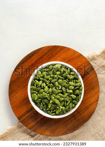 Pumpkin seeds. Still life for advertising photography for online store or marketplace. Peeled pumpkin seeds in plate on wooden board. Top view with copy space.