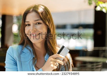 Positive smiling woman holding credit card, looking at camera on street, outdoors. Attractive female with beautiful hair posing for picture, e-commerce concept