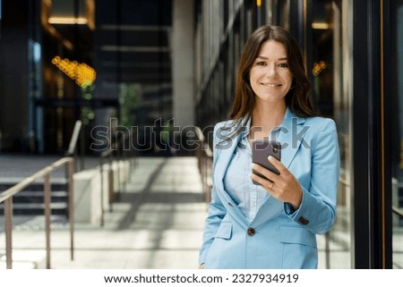 Portrait of beautiful smiling businesswoman wearing formal wear, business suit, holding phone, texting message, looking at camera, copy space. Attractive female online shopping, mobile banking Royalty-Free Stock Photo #2327934919