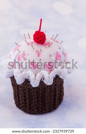 details of a cupcake-shaped pincushion, on a texturede background