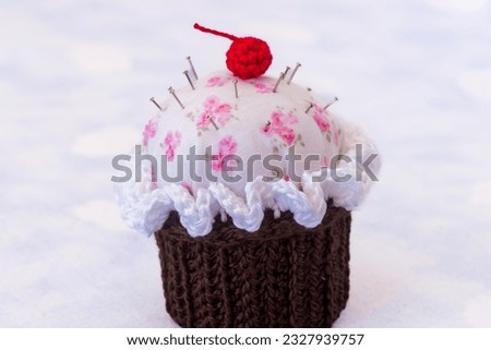 details of a cupcake-shaped pincushion, on a texturede background