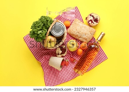 Wicker basket with tasty food for picnic, wine and glass on yellow background