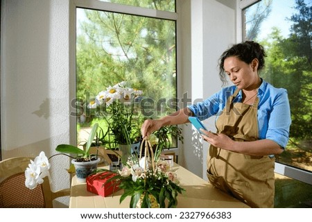 Pregnant woman florist entrepreneur, flower designer taking photo of a cute floral arrangement on smartphone in a floral design studio, dressed in beige apron. Creative occupation in pregnancy time