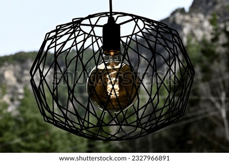 Ceiling chandelier with a mesh frame hangs against the backdrop of high mountains with trees in the background. nice view from the window. A high resolution.