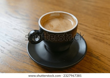 A black coffee cup with espresso coffee stands on a wooden table. perspective