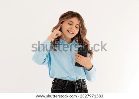 Image of a happy young beautiful woman posing isolated over white wall background listening music with earphones using mobile phone.