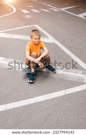 Outdoor activities for children. A cheerful young boy in bright clothes sits on a skateboard. Caucasian schoolboy on a walk. Top view