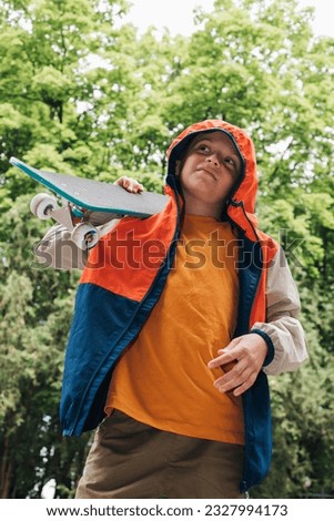 Outdoor activities for children. A cheerful young boy stay with a skateboard in public park. Caucasian schoolboy on a walk. Bottom view