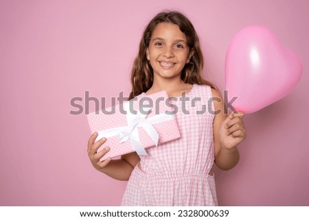Picture of happy little girl child standing isolated over pink background. Looking camera holding gift box surprise.