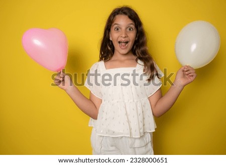 Adorable little child girl holding a bunch with inflatable balloons, isolated on yellow color background, confidently looking at camera. Emotions. Kids. International Children's day concept