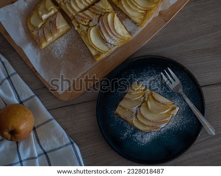 Apple vanilla squares. Homemade apple pie topped with slices of apples. Serving of delicious fruit vanilla cake on a dark plate with fork. Thin slices of apples are stuffed tightly and powdered sugar.