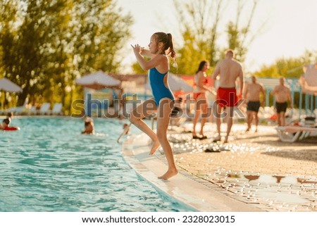 Teen girl jumps into the water from the side of the pool. swimming in the pool. concept of safe play in the water and learning to swim. Vacation with children. people in background are out of focus 