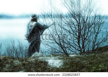 Norse woman looking out over fjord. Medieval clothing and closeness to nature evokes another time and world lost to us in our modern world. Creative coloring and textures evokes mysticism. Royalty-Free Stock Photo #2328025857